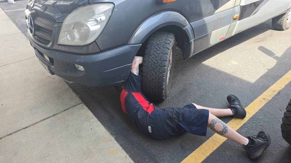 A technician working under an import van at PDQ Import Repair
